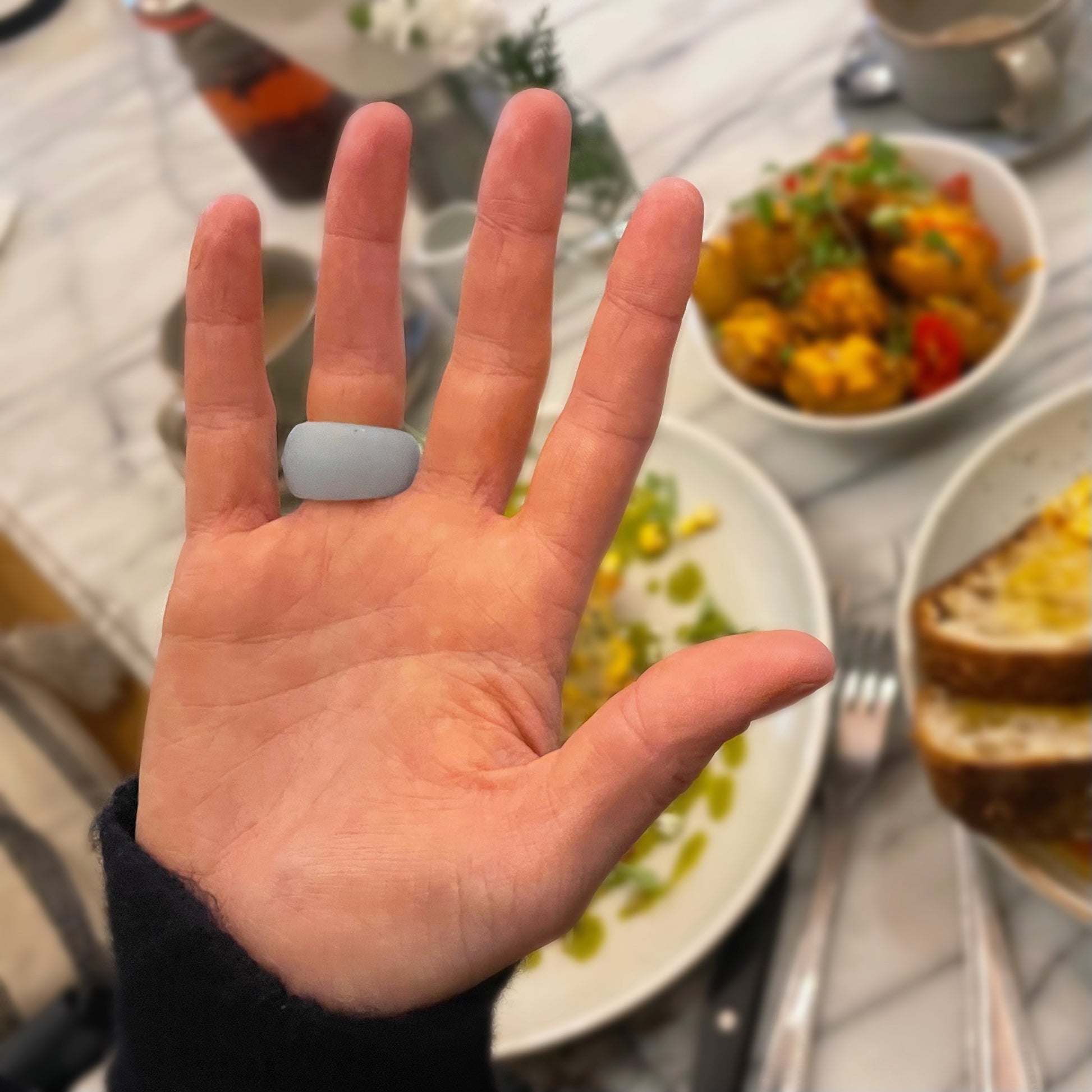 A woman's hand wears a blue ring protector, in the background is a restaurant table with food. 